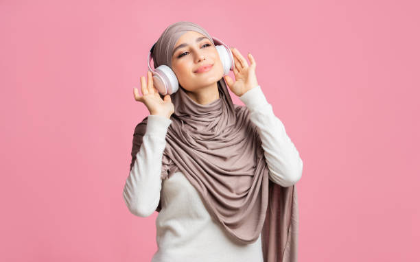 garota árabe alegre no hijab ouvindo música favorita com fones de ouvido sem fio - arab style audio - fotografias e filmes do acervo