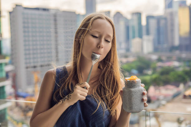 Young woman eating chia pudding on her balcony overlooking the big city Young woman eating chia pudding on her balcony overlooking the big city. eating chia seeds stock pictures, royalty-free photos & images