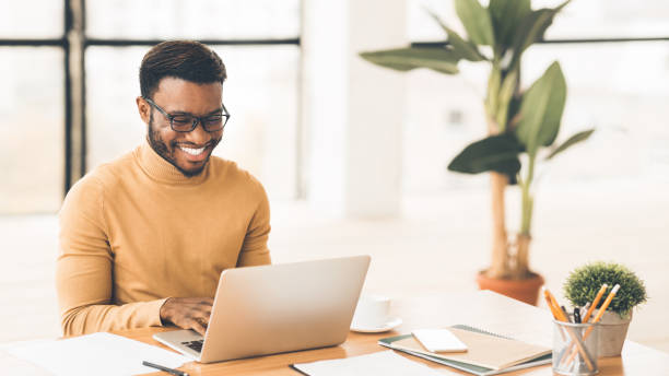 Headshot of handsome black guy using laptop Successful Freelancer. Happy afro man smiling and working on laptop in home office. Copyspace, panorama recruiter stock pictures, royalty-free photos & images