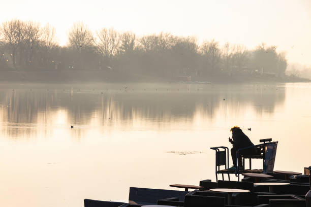 sagoma di una persona seduta sulla riva del fiume mentre guarda l'altra riva - quit lake foto e immagini stock