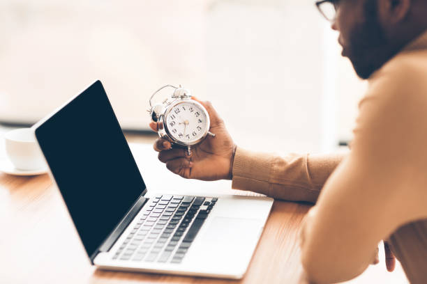 istock Unrecognizable afro businessman holding clock using laptop 1200940199