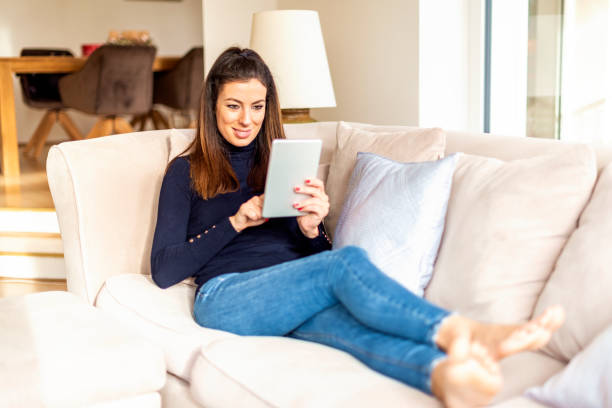 istock Happy woman using digital tablet while relaxing at home on the sofa 1200945794