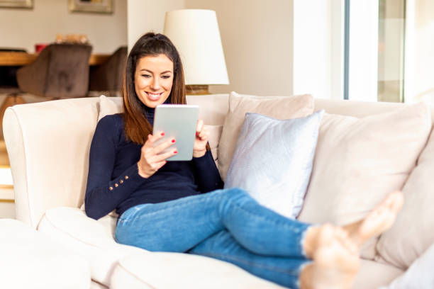 istock Happy woman using digital tablet while relaxing at home on the sofa 1200945796