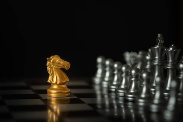 Gold knight chess in battle. Gold knight chess stands on chessboard in front of opponents on dark background with copy space. Business strategy, planning, decision, and competition concept. knight chess piece photos stock pictures, royalty-free photos & images