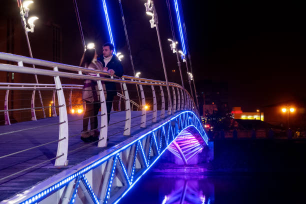 Man and woman are talking while standing on a luminous bridge at night