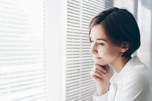 istock Woman staring out of window blinds 1200950266