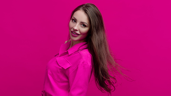 Cute and cheerful young brunette in a pink suit on a pink background. Positive young woman in a bright image, copy space