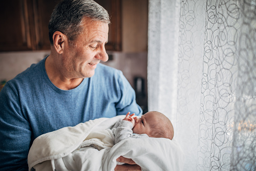 Grandfather holding his newborn grandson and looking him with love