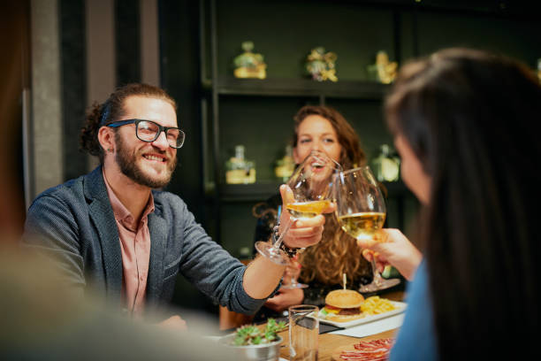 istock Best friends sitting in restaurant for dinner and making a toast with white wine. On table is food. 1200951893