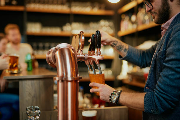 istock Tattooed caucasian barman pouring beer while standing in pub. Selective focus on hand. 1200953370