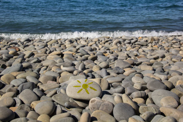 Bright sun painted on pebble. Pebbles and sea background in summer