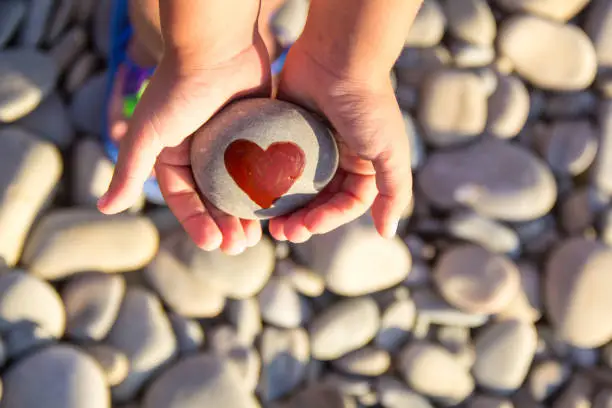 Photo of pebbles with a painted heart in the hands of a child on the background of a pebble beach