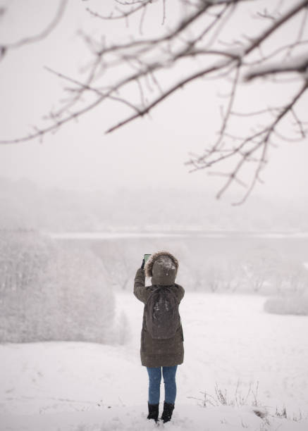istock Woman photographing forest with cell phone during snowfall 1200955264