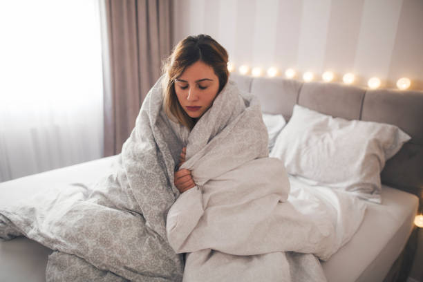istock Sick girl sitting on the bed wrapped in blanket. 1200961177
