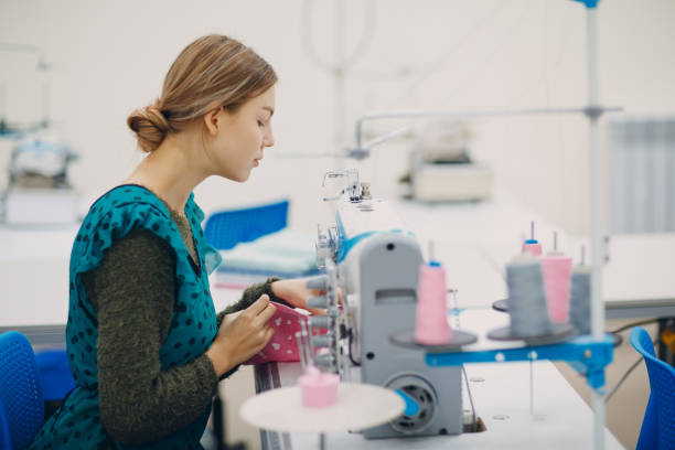 istock Young beautiful seamstress sews on sewing machine in factory 1200967150