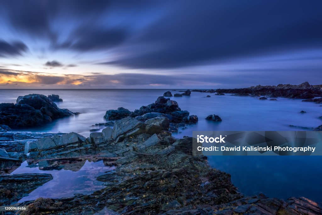 Twilight begins yielding to daylight at rocky coastline Twilight begins yielding to daylight at rocky coastline with blurred water and sky, long exposure photography. Northern Ireland Beach Stock Photo