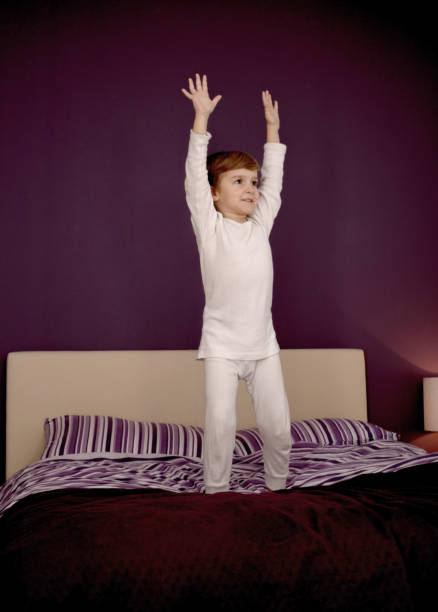 istock Small boy with arms raised jumping on the bed. 1200968565