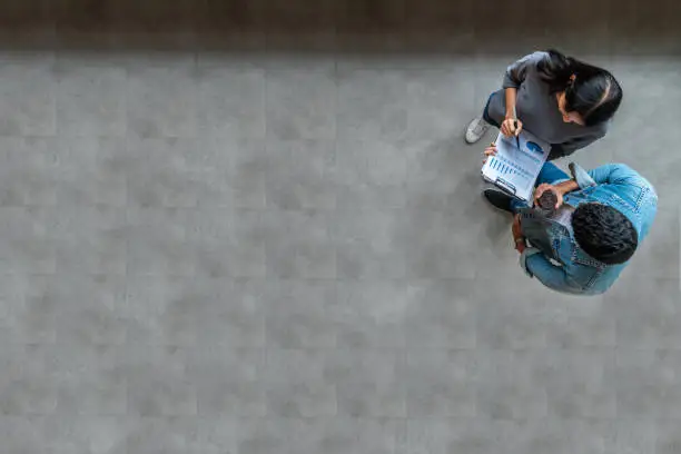 Photo of Top view of young asian business team standing, talking and reporting with annual report document in modern workplace. Above view of casual creative team discussion with report performance.