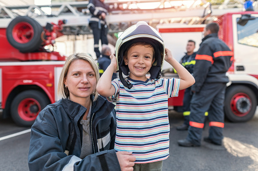 Cheerful little boy with his mother firefighter playing with the safety helmet
