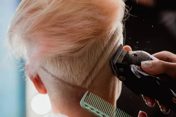 Photo of Hairdresser machine cuts woman client. A short haircut, shaved temple and a drawing on the hair.