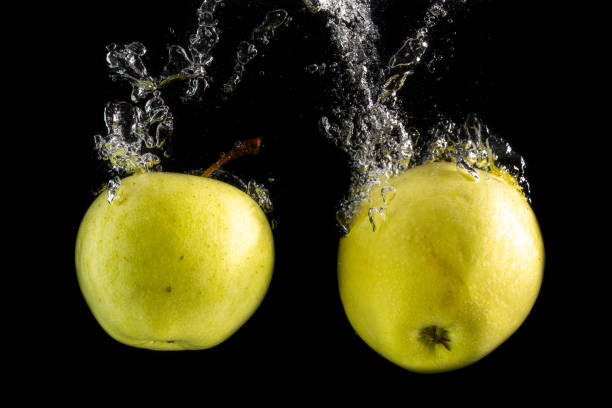 istock Two green apples falls into the water with splashes and bubbles on a black background 1200983696