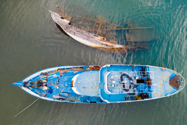 Old boat vs boat Sunken boat next to a boat. Taken via drone fishing boat sinking stock pictures, royalty-free photos & images