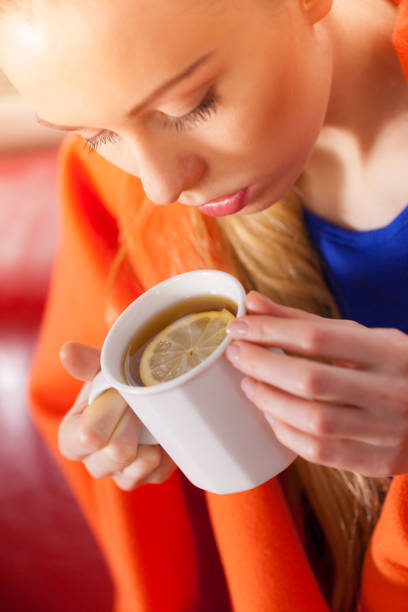 istock Woman lying on sofa under blanket drinking tea 1200989140