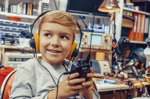 Happy kid with headphones talking over CB radio in a workshop.
