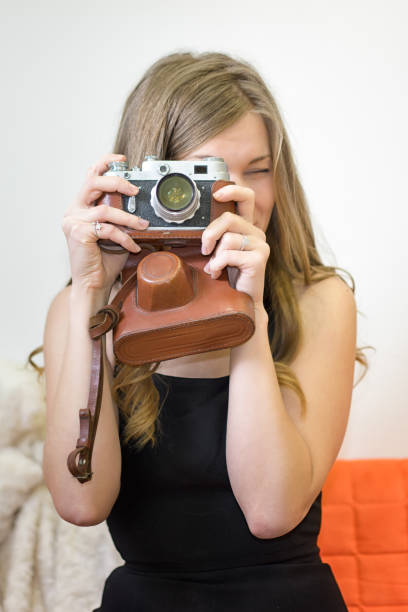 istock Young woman holds a retro camera in her hands, squints, and makes a photo. 1200995480