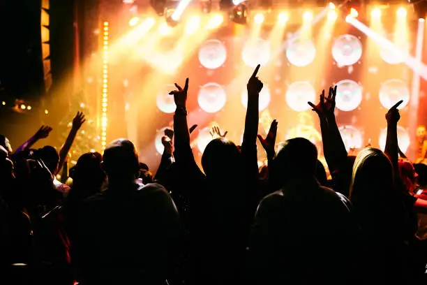 Photo of Crowd at a music concert, audience raising hands up in front of bright stage lights.
