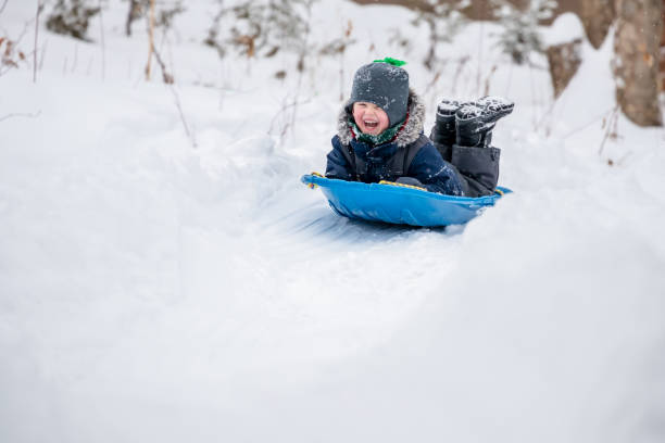 mały chłopiec przesuwne w śniegu na zewnątrz w zimie - sleding zdjęcia i obrazy z banku zdjęć
