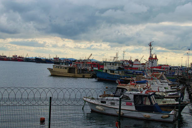 イスタンブールの係留漁船や船と港。男はボートに乗って出航する。背景の都市景観。ドラマチックな冬の空。イスタンブール(トルコ) - looking at view on top of nautical vessel high section ストックフォトと画像
