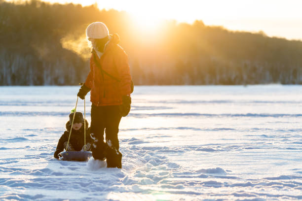 istock Mother Pulling Son on Sled on Frozen Lake in Winter at Sunset 1200997983