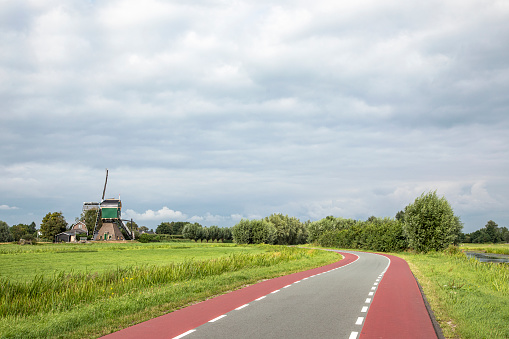 Road to mill in the netherlands with red cycle path on both sides, perspective, under dark cloudy sky