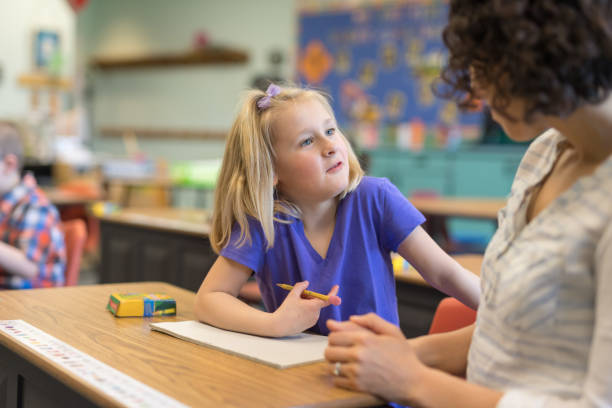 istock Elementary-age girl talking with her teacher in the classroom 1201002521
