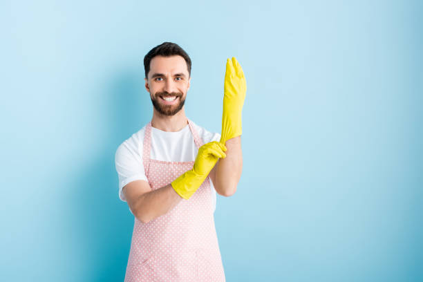 istock cheerful man in apron wearing rubber gloves on blue 1201003502