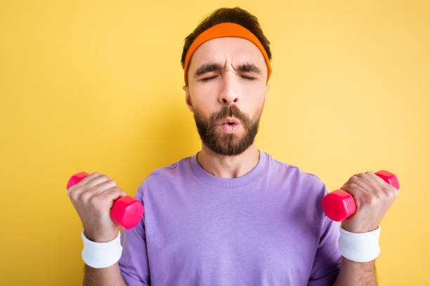 istock bearded sportsman breathing while exercising with small dumbbells isolated on yellow 1201003513