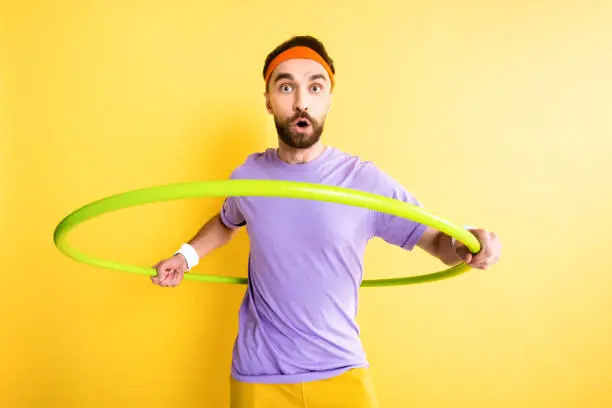 surprised sportsman exercising with hula hoop isolated on yellow