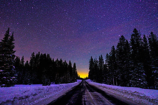 Straight Road at Night in Winter Under Bright Stars - Desolate road with dark sky and orange glow on the horizon. Astrophotography landscape.