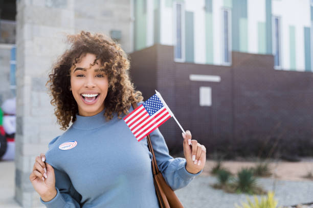 Mid adult woman displays "I Voted" sticker and American flag Afte voting, the mid adult woman displays her "I Voted" sticker and a small American flag. citizenship stock pictures, royalty-free photos & images