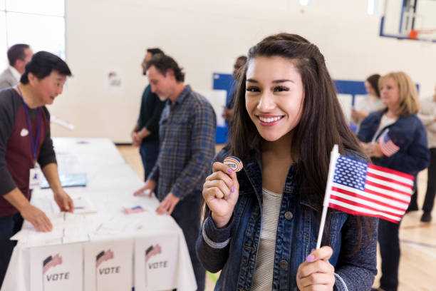 happy young woman holds up "i voted" sticker and flag - jovens a votar imagens e fotografias de stock