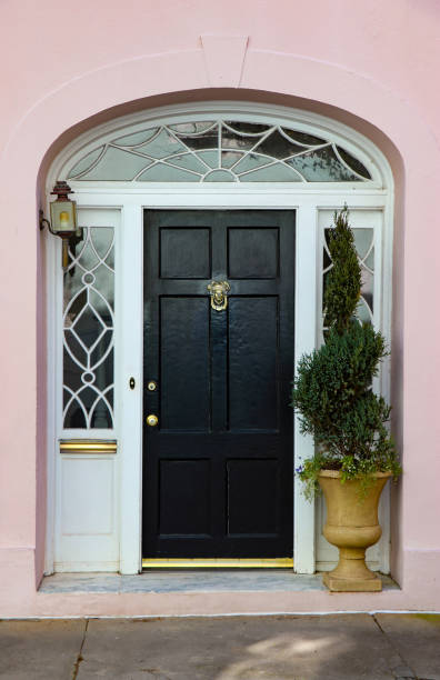 Entrance to an old house with decorative cut glass windows, pink stucco walls, and a black door with fancy brass knocker. stock photo