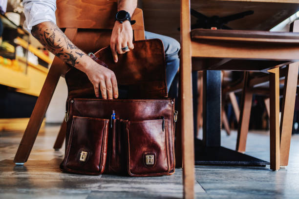 Caucasian businessman with tattoo taking out tablet from his leather bag. Caucasian businessman with tattoo taking out tablet from his leather bag. briefcase photos stock pictures, royalty-free photos & images