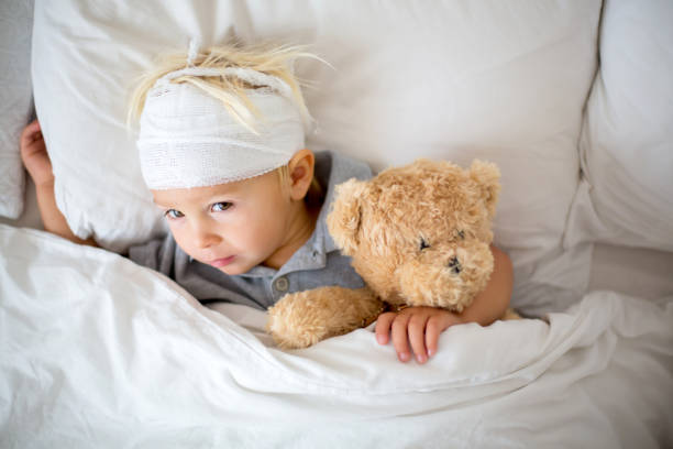 niño pequeño con lesión en la cabeza, acostado en la cama, cansado - child physical injury teddy bear wound fotografías e imágenes de stock