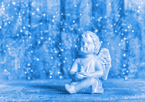 Blue Christmas decoration. Little guardian angel with festive lights background