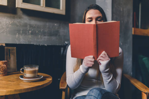 istock Young woman drinking coffee and reading book in cafe 1201040554