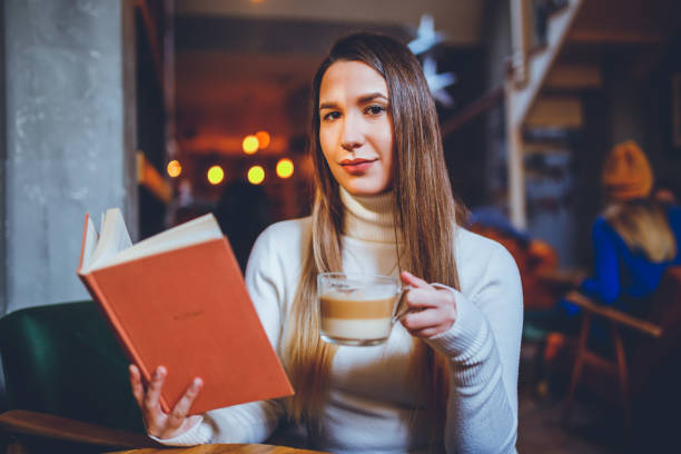 istock Young woman drinking coffee and reading book in cafe 1201040635