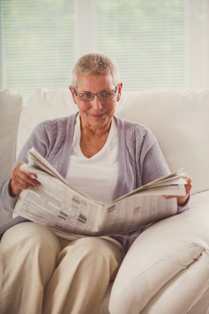 istock Smiling senior woman reading newspaper 1201050048