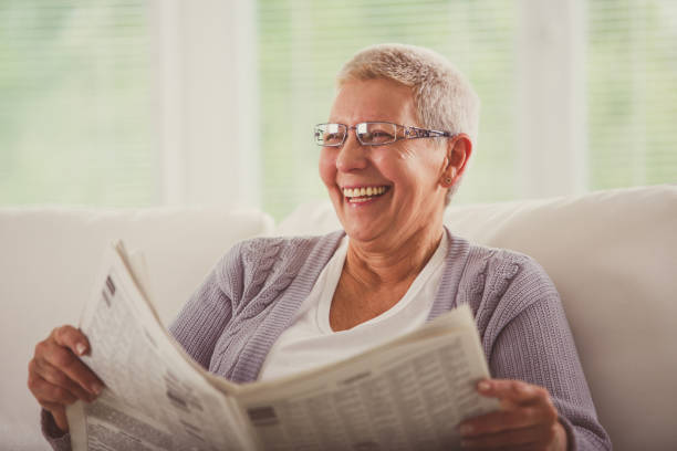 istock Senior woman laughing while reading newspaper 1201050052
