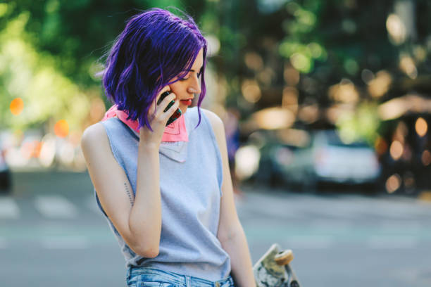 Skater girl talking on the phone in the street in Buenos Aires Young skater woman talking on the smartphone in the street and holding her skateboard, Buenos Aires, Argentina. purple hair stock pictures, royalty-free photos & images